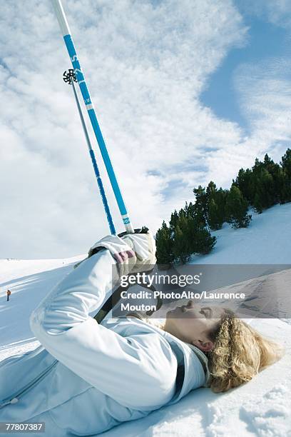 young female skier lying on ground, holding up ski sticks, eyes closed - ski closeup stock-fotos und bilder