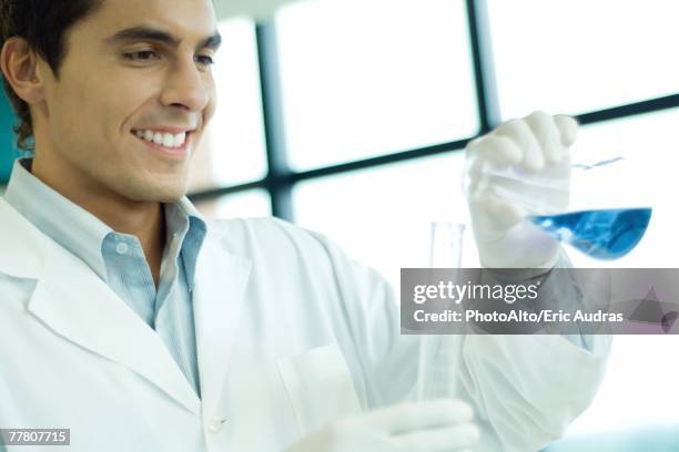 male scientist transfering liquid from flask to cylinder, smiling - transfering stock pictures, royalty-free photos & images