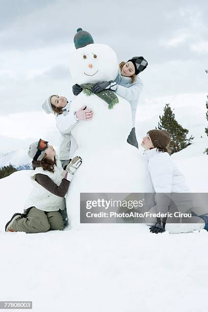 young female friends grouped around snowman - traditional parka stock pictures, royalty-free photos & images