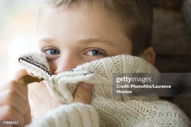 boy zipping collar of wool sweater over face, close-up - sweater stockfoto's en -beelden