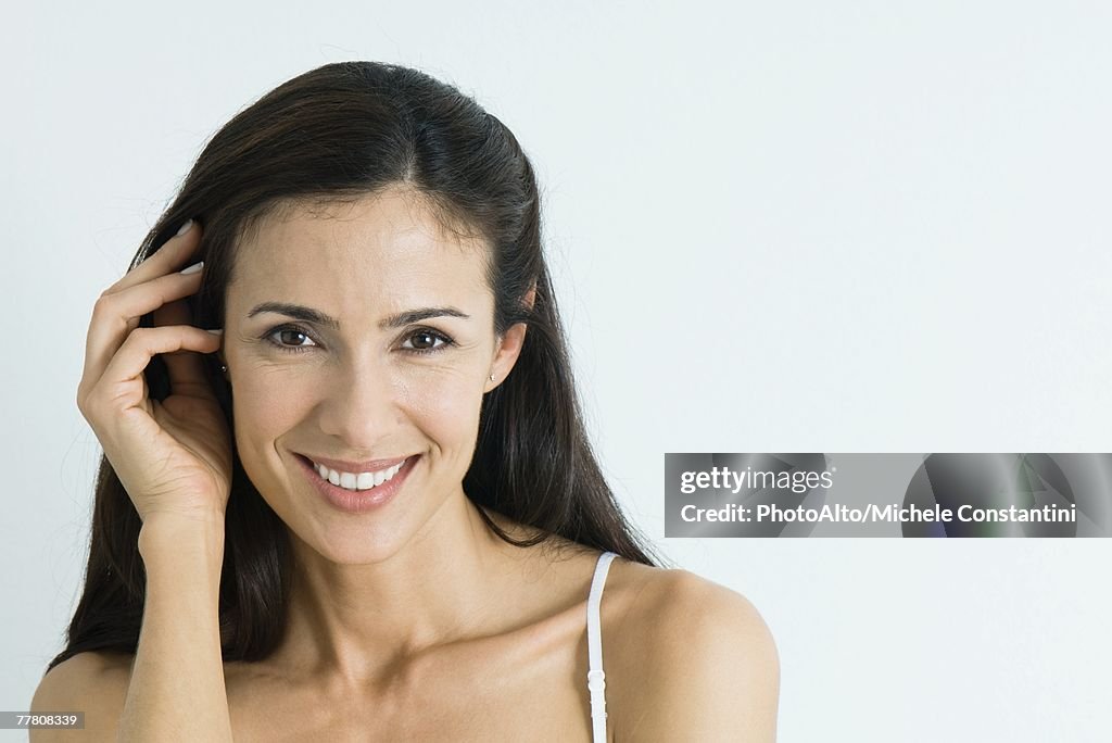 Woman, pushing hair back, smiling at camera, portrait