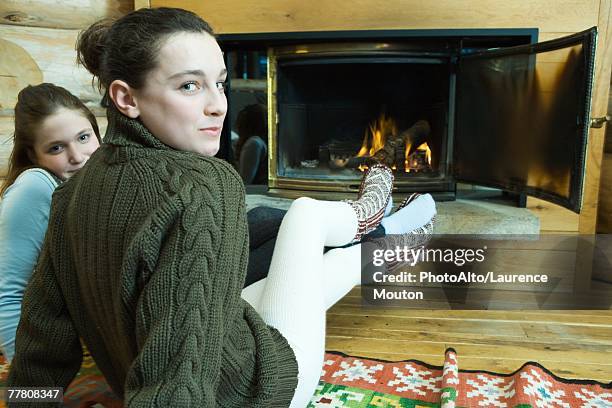 two teenage girls sitting by fireplace, smiling at camera - teen girls in tights stock-fotos und bilder