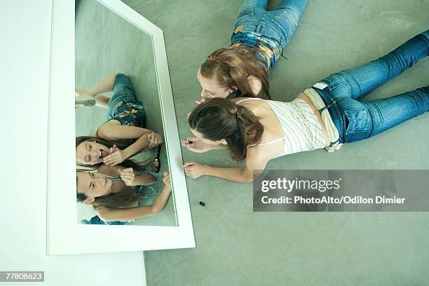 two young friends lying on ground, looking at selves in mirror, holding lipstick, view from directly above - woman lipstick rearview stock pictures, royalty-free photos & images