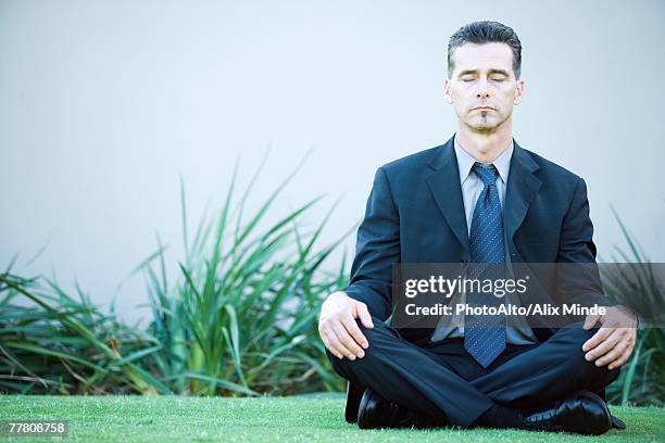 businessman sitting on ground outdoors, meditating, eyes closed - schneidersitz stock-fotos und bilder
