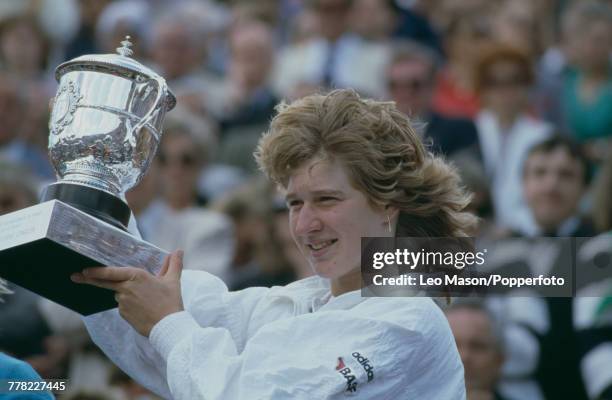German tennis player Steffi Graf holds up the trophy after beating American tennis player Martina Navratilova 6-4, 4-6, 8-6 to win the final of the...