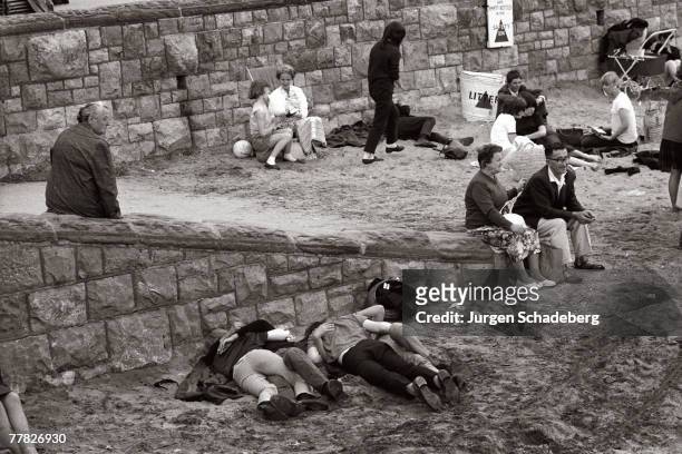 Young couples huddle together at the beach in Britain, circa 1965.