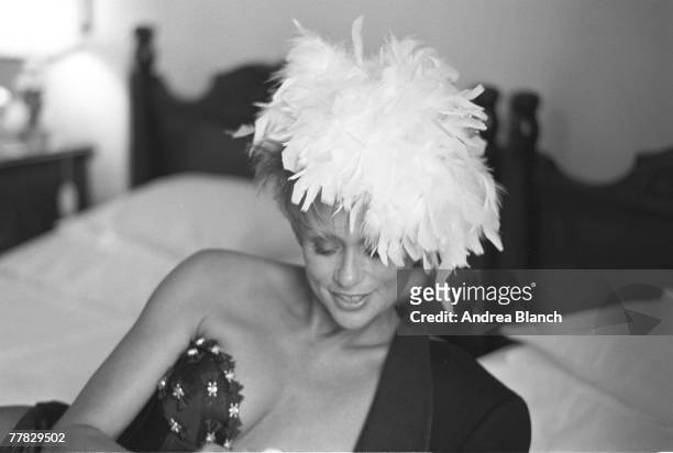 American actress and model Lauren Hutton as she leans on one arm on a bed, dressed in a bustier and feather headpiece during a photohoot for Harper's...