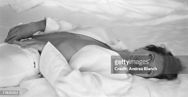Portrait of American fashion model and actress Carre Otis as she lies on her back, her shirt unbuttoned, late 1980s or 1990s.