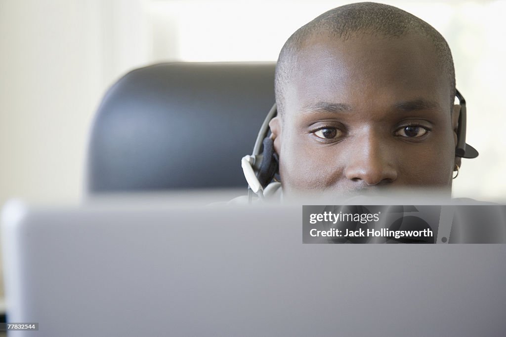Male customer service representative wearing a headset in front of a laptop