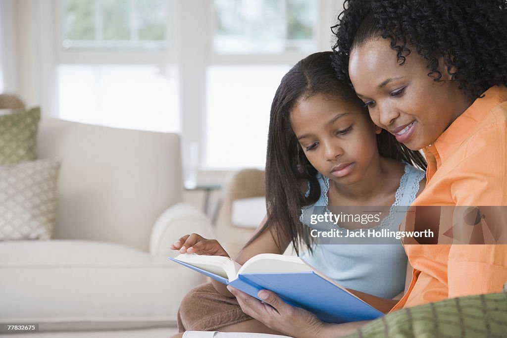 Side profile of a mid adult woman reading a book with her daughter and smiling