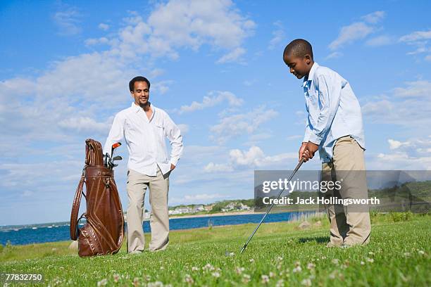 side profile of a boy playing a golf with his father standing in the background - putting clothes son stock pictures, royalty-free photos & images