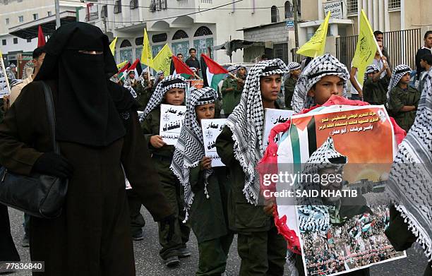 Palestinian woman walks next to children dressed as late leader Yasser Arafat marching during a rally marking the third anniversary of his death in...