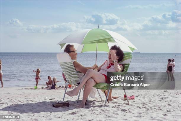 Two women sitting in deckchairs under a parasol on Rockaway Beach, Queens, New York, September 1986.