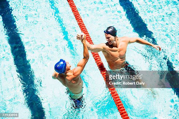 two swimmers in a pool joining hands - team player stockfoto's en -beelden