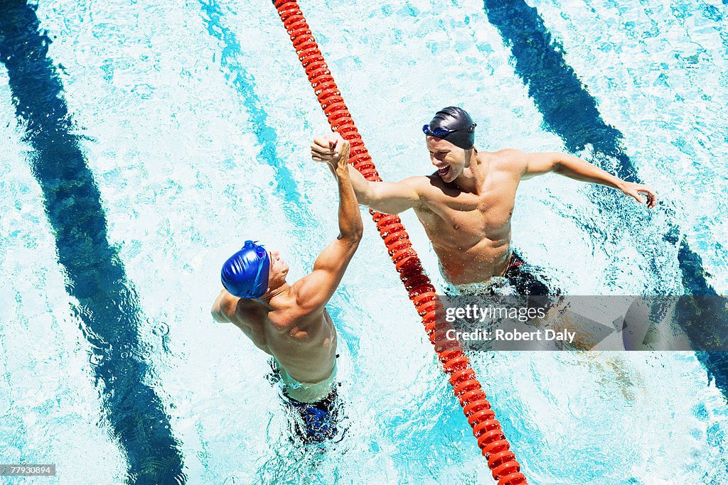Two swimmers in a pool joining hands