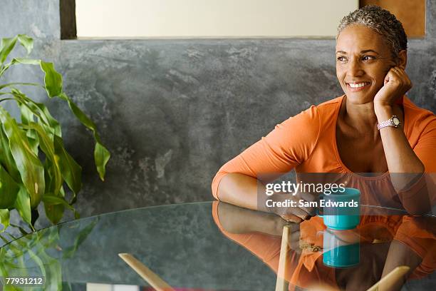 woman sitting at a table with a mug smiling - alleen oudere vrouwen stockfoto's en -beelden