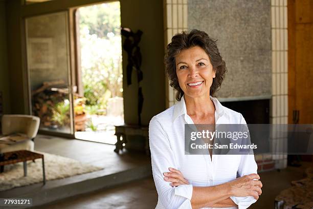 mujer de pie con los brazos cruzados sonriendo en casa moderna - baby boomer fotografías e imágenes de stock