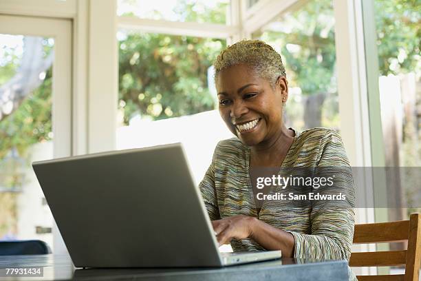 woman on laptop at a table smiling - samuser stock pictures, royalty-free photos & images