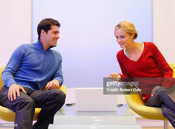 man and woman sitting in chairs with laptop between them - side table stock pictures, royalty-free photos & images