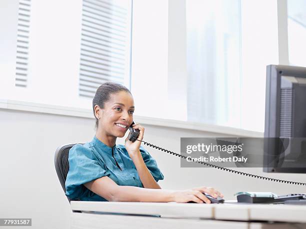geschäftsfrau am telefon auf einem computer im büro - festnetztelefon stock-fotos und bilder