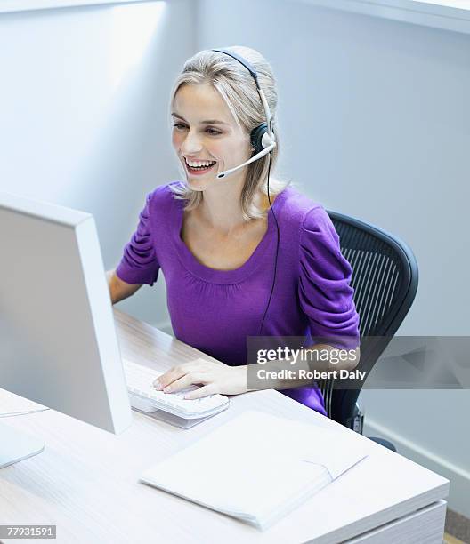 businesswoman wearing a headset at her desk smiling - computer headset stock pictures, royalty-free photos & images