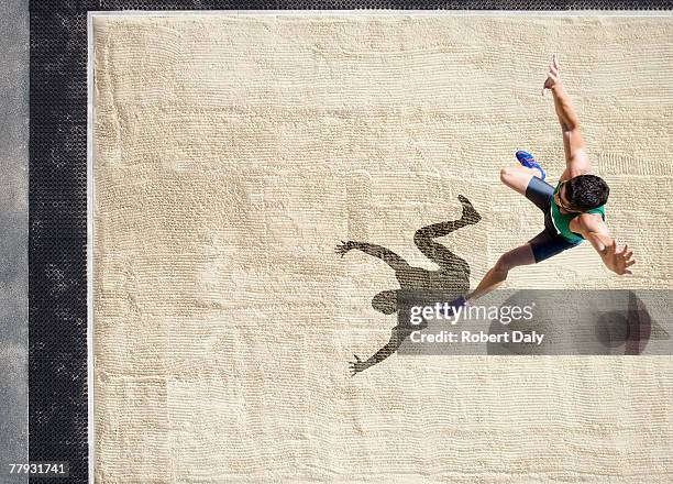 athlete doing a long jump into a sandpit - verspringen stockfoto's en -beelden