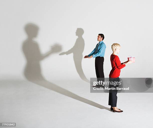 businessman and woman standing so shadows look like she's giving him a gift - illusie stockfoto's en -beelden