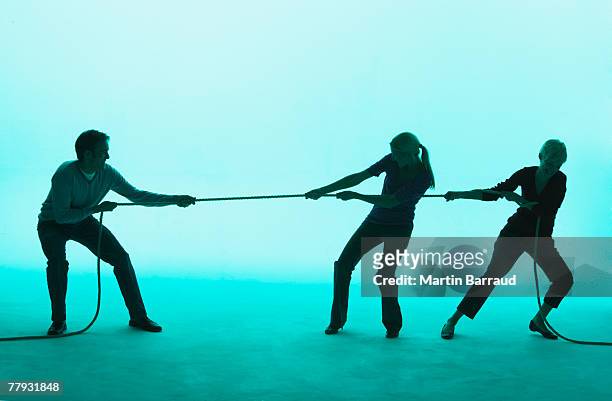 hombre y dos mujeres jugando tug de guerra - lucha de la cuerda fotografías e imágenes de stock
