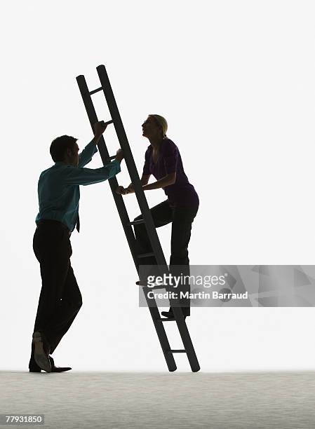 man holding a ladder while a woman climbs it - moving up the ladder stock pictures, royalty-free photos & images