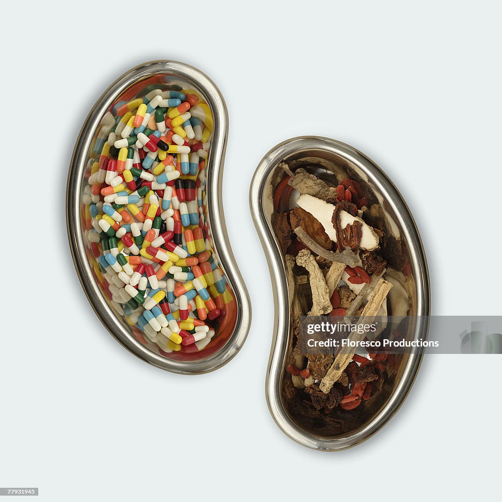 A kidney shaped bowl of pills beside a bowl of herbs