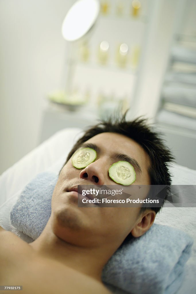 Man on massage table with cucumbers over eyes