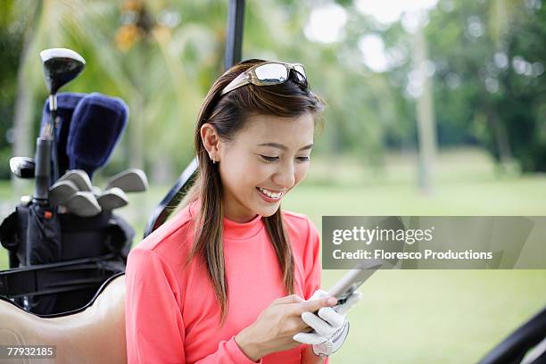 woman in a golf cart looking at her mobile phone - golfhandschuh stock-fotos und bilder