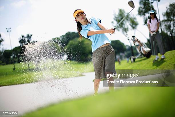 woman playing golf with woman in background - golf bunker stock-fotos und bilder