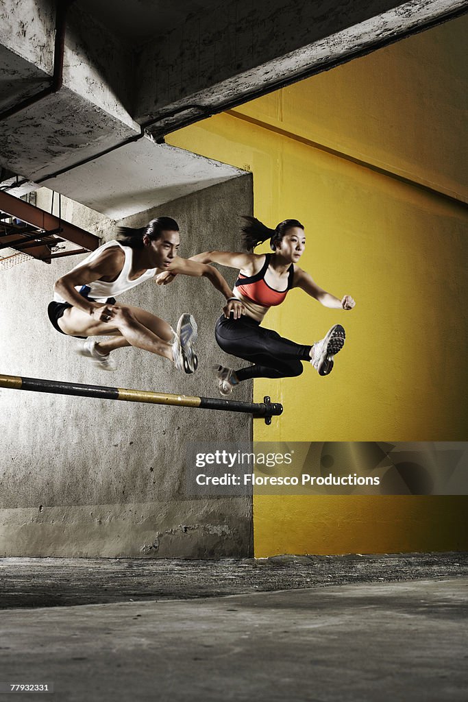 Two athletes jumping a parking garage barrier