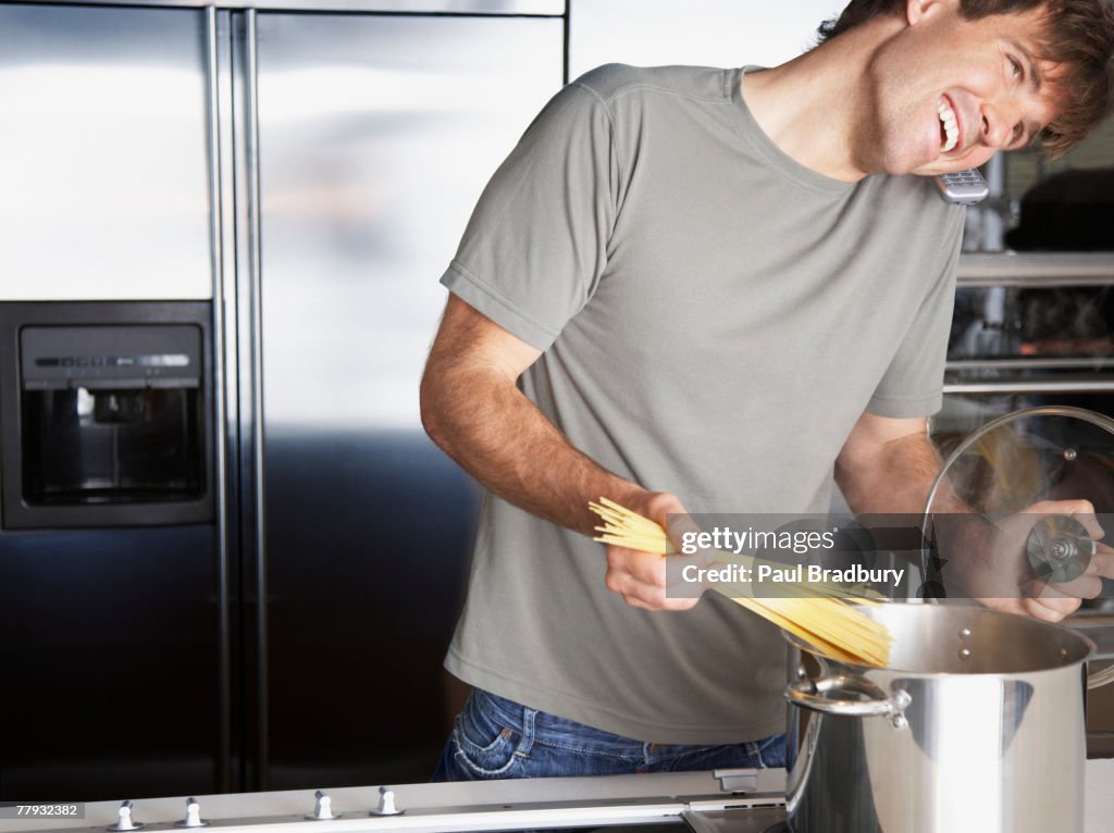 Man putting pasta into a cooking pot while on telephone