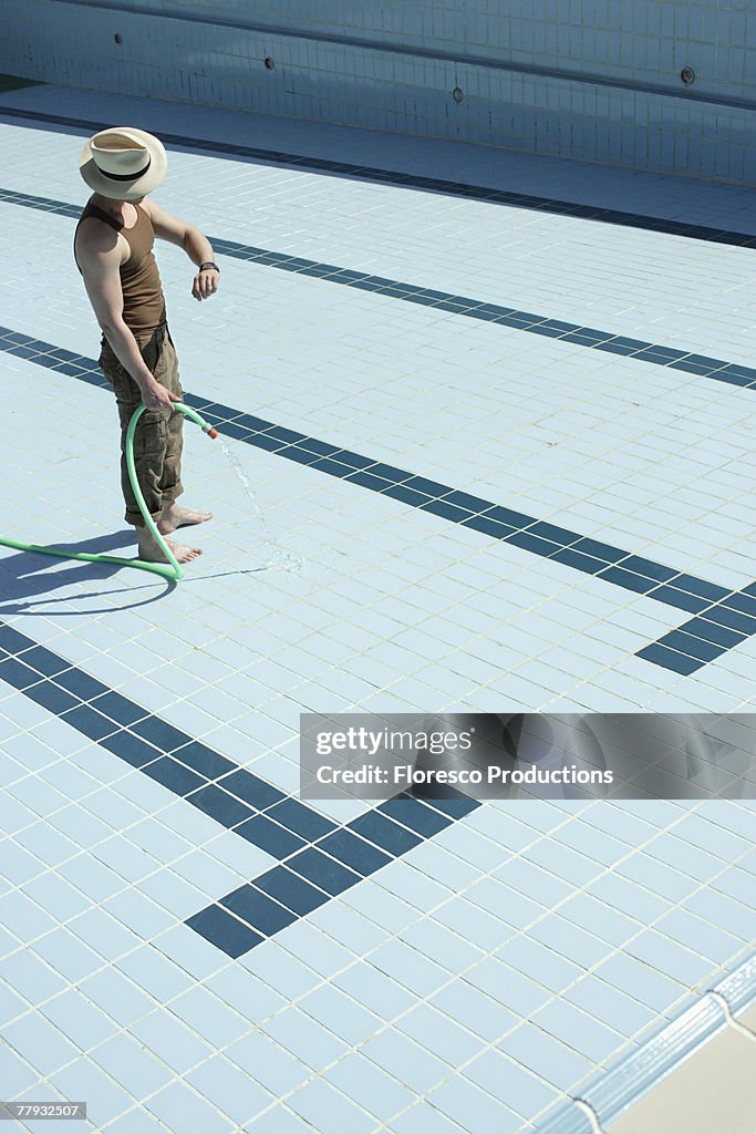 Man standing in empty pool with hose