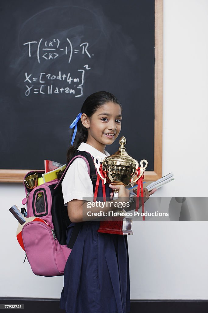 Girl with trophy by blackboard in classroom