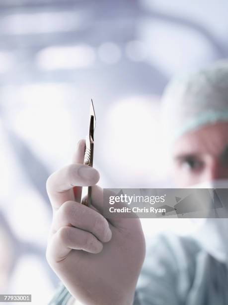 doctor holding a scalpel in foreground - scalpel stock pictures, royalty-free photos & images