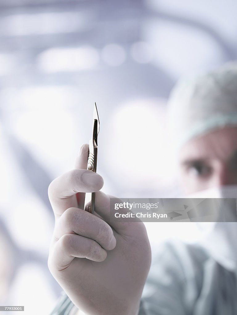 Doctor holding a scalpel in foreground