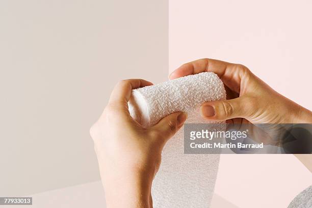 a roll of gauze sitting being rolled back up by two hands - bandage stock pictures, royalty-free photos & images