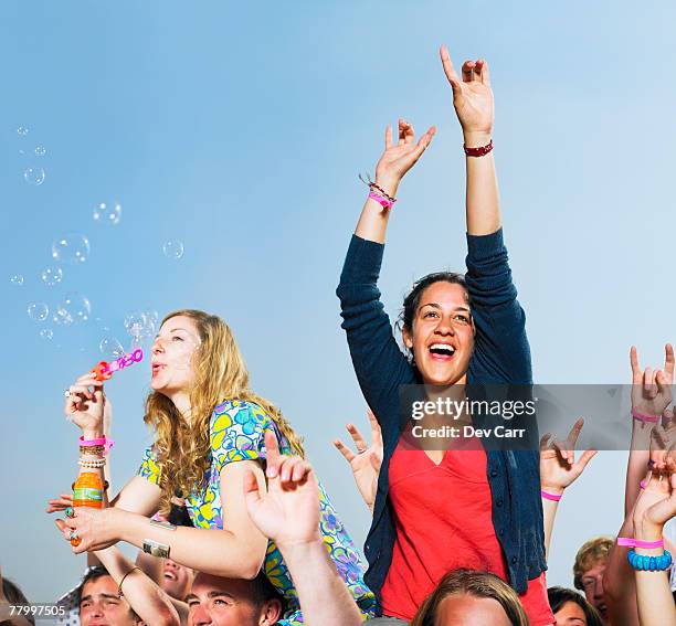 two girls sitting on shoulders in a crowd blowing bubbles - bubbles outdoor stock pictures, royalty-free photos & images