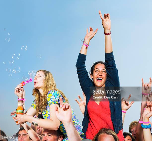 two girls sitting on shoulders in a crowd blowing bubbles - park festival bildbanksfoton och bilder