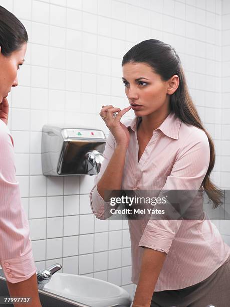 woman reflected in office washroom mirror applying make-up - office bathroom stock-fotos und bilder