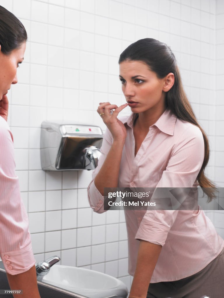 Woman reflected in office washroom mirror applying make-up