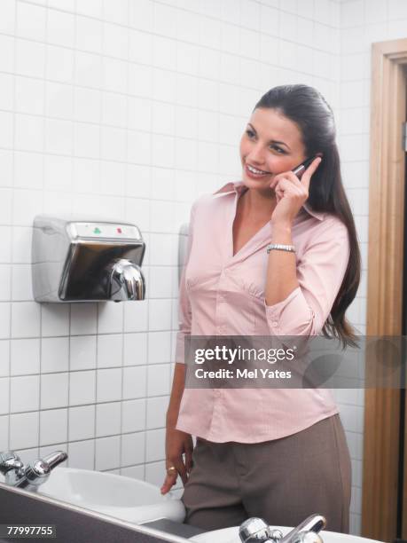 woman reflected in office washroom mirror using mobile phone - hand dryer stock pictures, royalty-free photos & images
