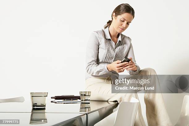 young business woman seated on desk sending text message. - feature phone stockfoto's en -beelden