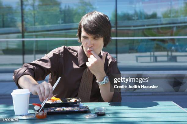 businessman on table in front of office outside with sushi lunchbox and sticks licking off his finger. - licking finger stock pictures, royalty-free photos & images