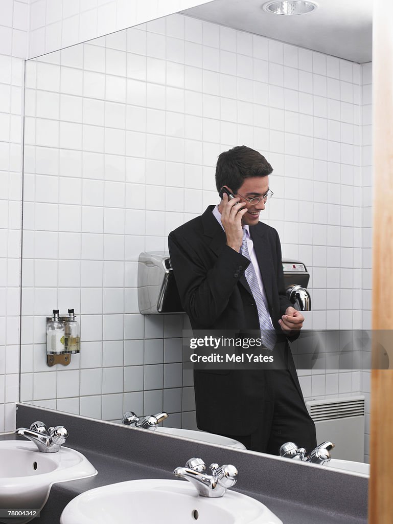 Man reflected in office washroom mirror using mobile phone