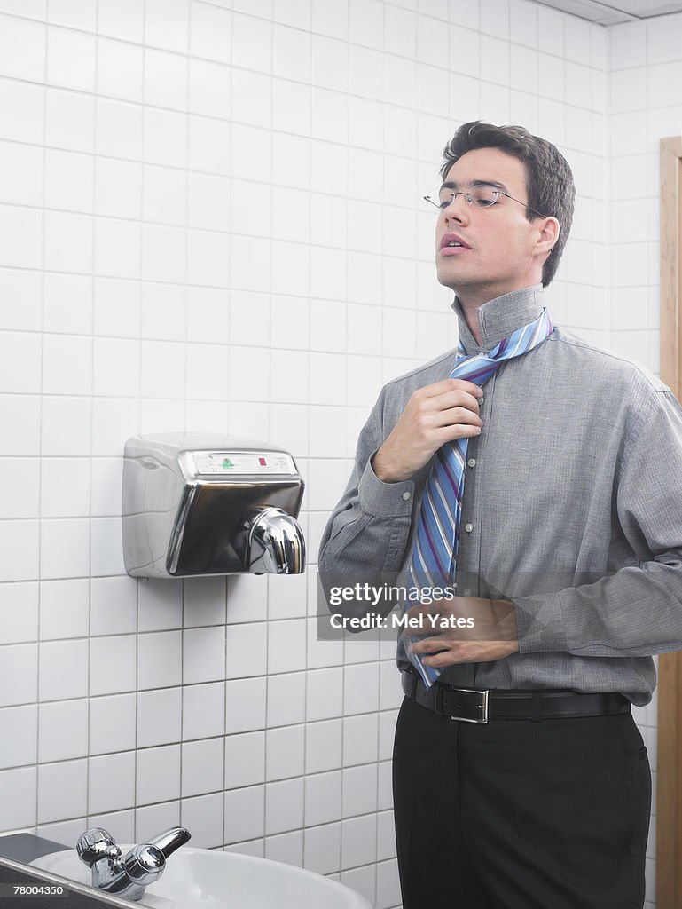 Man reflected in office washroom mirror doing up his tie