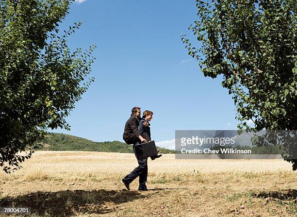 businessman carrying another businessman through orchard. - piggyback stock pictures, royalty-free photos & images